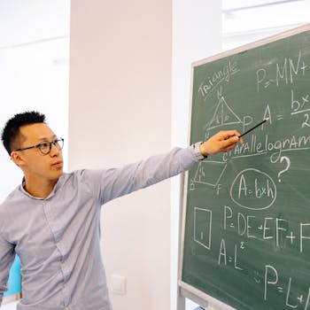 pexels-photo-8617769-8617769 A male teacher points at equations on a blackboard during a lesson in a classroom setting.