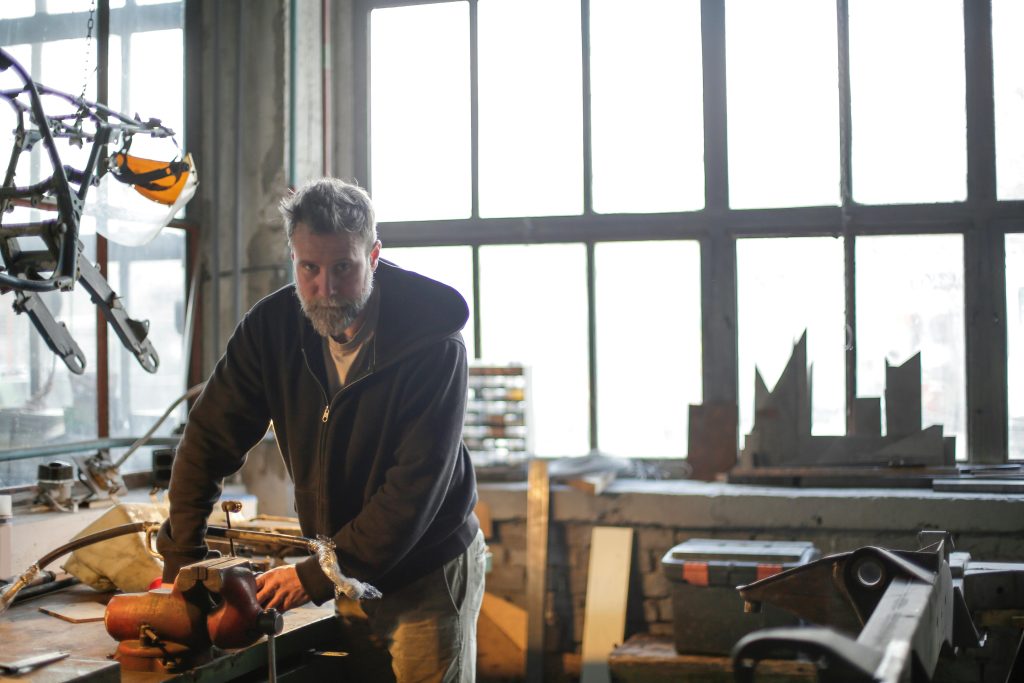 pexels-photo-3855479-3855479 A bearded man concentrates on a repair task in a well-lit workshop, surrounded by tools.